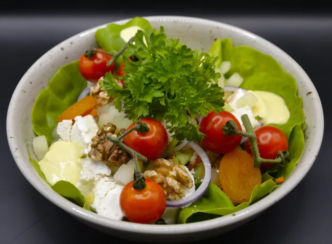Salade met kerstomaten, walnoten, uienringen, sla, kaas, gedroogde abrikoos en peterselie.