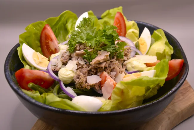 Salade met sla, tomaat, ei, tonijn, uienringen en peterselie in een zwarte kom.